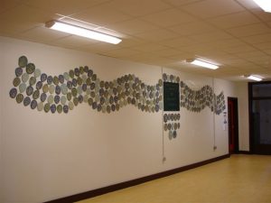 The finished project exhibited over two walls. (Dimensions - 7m x 1.3m) Public Art Project 2006 by ceramic artist Michelle Maher & the children, staff & parents at St. Patrick's N.S., Diswellstown, Dublin 15 - to commemorate the opening of their new school. Working in collaboration we created a wall piece entitled 'When the hand was lifted from the clay', it comprised of the handprints of almost 450 participants and was installed in the foyer of the new school building. www.ceramicforms.com